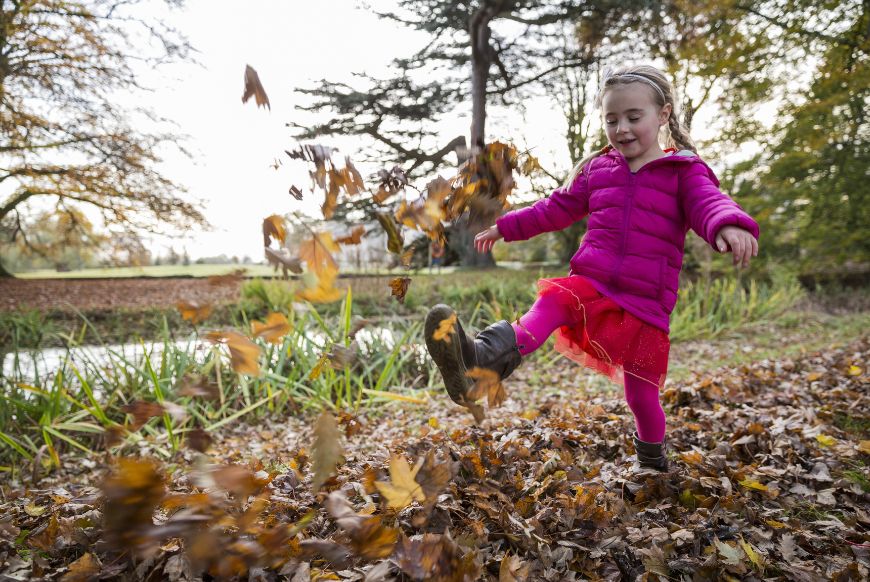 a girl in a pink coat is kicking orange leaves